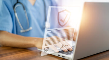 A doctor with a stethoscope sitting in front of.a laptop with a digital cybersecurity certificate