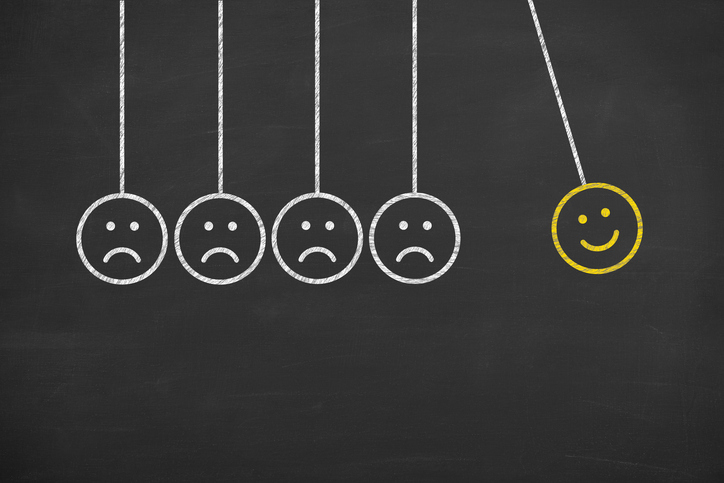 Hanging emoticons against a black board with one smiley face emoticon.